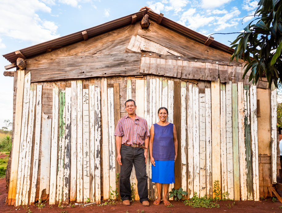 Indigenous Brazilian couple pose in front of rustic wooden shed outside Dourados, Brazil